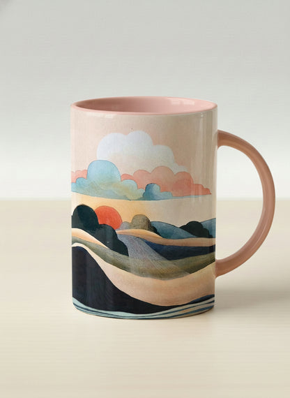hero mug | Sunset at the River mug rolling hills and dark treetops beneath a soft peach sky with blush and teal clouds and a glowing setting sun, warm peach interior and handle, by KikaG - Gallery By Inhesion