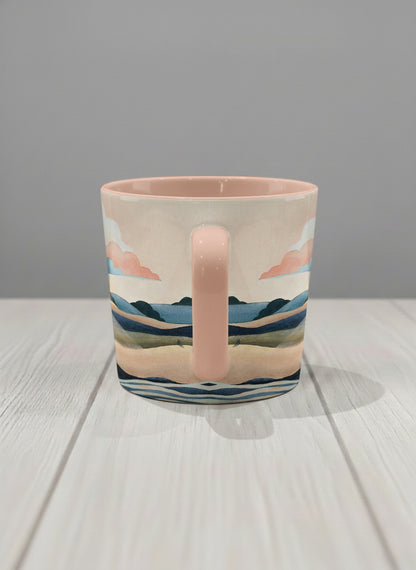 conical mug | Sunset at the River side view mug rolling hills and dark treetops beneath a soft peach sky with blush and teal clouds and a glowing setting sun, warm peach interior and handle, by KikaG - Gallery By Inhesion