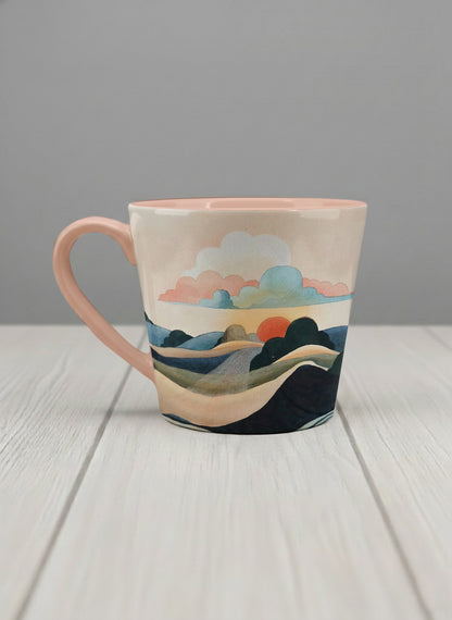 conical mug | Sunset at the River left view mug rolling hills and dark treetops beneath a soft peach sky with blush and teal clouds and a glowing setting sun, warm peach interior and handle, by KikaG - Gallery By Inhesion